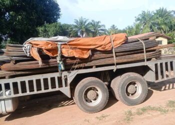 A flatbed truck carrying stacked construction materials parked on a dirt road.
