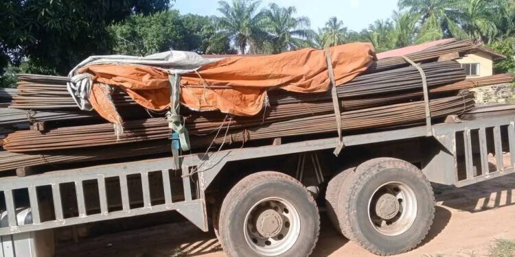 A flatbed truck carrying stacked construction materials parked on a dirt road.