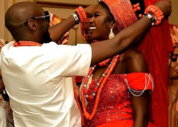 A man placing traditional jewelry on a smiling woman during a vibrant African wedding ceremony