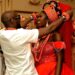 A man placing traditional jewelry on a smiling woman during a vibrant African wedding ceremony