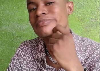 A young man identified as J. Christian Kargbo Jr., also known as MC J Christ, posing for a photo against a green wall before his arrest in a Bong County rape case