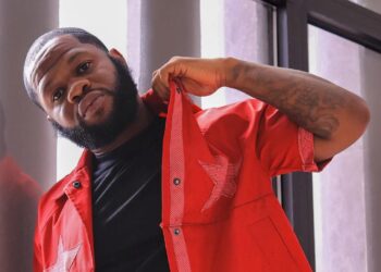 Liberian rapper Bucky Raw poses in a red jacket during a photoshoot, highlighting his public image amid ongoing discussions about mental health and his legal troubles.