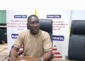 A man seated at a conference table speaking during an Integrity Watch Liberia press briefing on the proposal to add 14 new legislative seats.