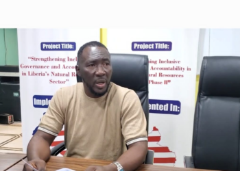 A man seated at a conference table speaking during an Integrity Watch Liberia press briefing on the proposal to add 14 new legislative seats.