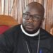 Rev. F. Philip L. Nushann Jr. seated indoors during the national Access to Justice conference, wearing clerical attire and speaking on justice reform initiatives.