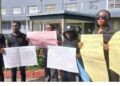 LINA employees hold protest placards outside the Legislature, calling for an audit and highlighting the lack of laptops, internet, and basic tools at the state news agency.