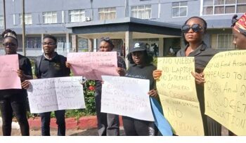 LINA employees hold protest placards outside the Legislature, calling for an audit and highlighting the lack of laptops, internet, and basic tools at the state news agency.