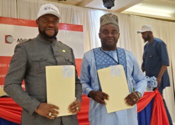 Two officials, CSA Director General Dr. Josiah Joekai Jr. and Afriland CEO Michel Doriand Pedie, hold signed partnership documents during the launch of the new salary advance and long-term loan program for Liberian civil servants