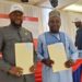 Two officials, CSA Director General Dr. Josiah Joekai Jr. and Afriland CEO Michel Doriand Pedie, hold signed partnership documents during the launch of the new salary advance and long-term loan program for Liberian civil servants