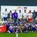 imba District #8 football team and officials pose with the championship trophy, medals, and a ceremonial check after winning the 2025 ArcelorMittal Cup in Ganta.
