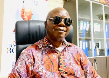 A man wearing sunglasses and a patterned shirt seated in an office, identified as UP Margibi fundraising chair Ben A. Fofana.