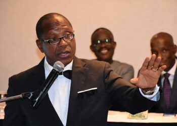 Moses D. Sandy delivering remarks at a podium during a formal event, addressing concerns about President Boakai’s handling of the Foya presidential villa project.