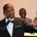 Moses D. Sandy delivering remarks at a podium during a formal event, addressing concerns about President Boakai’s handling of the Foya presidential villa project.