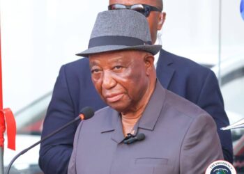 President Joseph Boakai speaking at a podium wearing a gray suit and hat during an official proclamation ceremony