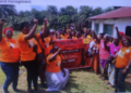 Group of women wearing orange shirts gathered outdoors holding a banner during a Women’s Land Rights Taskforce awareness event