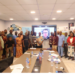 Group of workshop participants standing around a conference table during a fisheries management meeting in Monrovia with a virtual speaker displayed on a screen