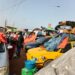 Liberian commuters at a Monrovia bus terminal as taxis and buses continue charging old fares despite the government’s October 2025 transport fare reduction.