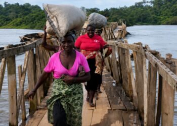 Residents gather near the collapsed temporary Payneberry Bridge in Buchanan, Grand Bassa County, after floodwaters swept away the pedestrian crossing.
