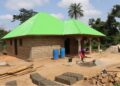 A beneficiary stands beside a house built with proceeds from the Salayea Community Forest village savings and loan scheme in Lofa County.