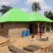 A beneficiary stands beside a house built with proceeds from the Salayea Community Forest village savings and loan scheme in Lofa County.