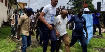 Police escort Rep. Thomas Romeo Quioh through the University of Liberia’s Capitol Hill campus as students gather nearby