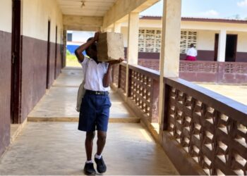 Student carrying concrete block to a classroom at J.W.A. Richards School in Louisiana Township, Liberia.