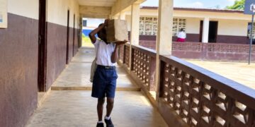 Student carrying concrete block to a classroom at J.W.A. Richards School in Louisiana Township, Liberia.